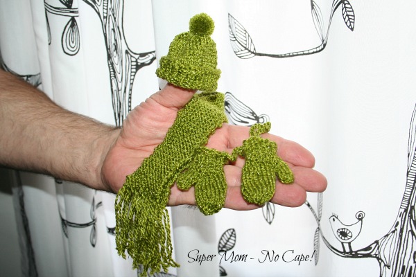Photo of hand holding green hat, scarf and mittens.