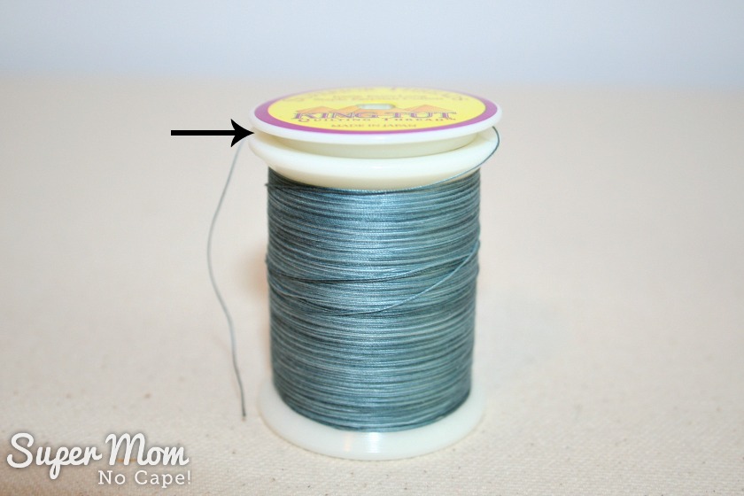 King Tut spool of thread with arrow showing how the top of the spool pops up