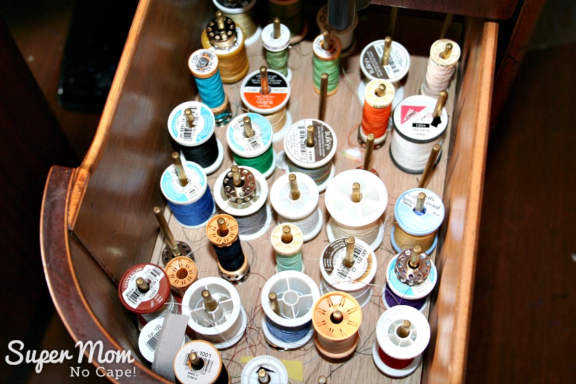 Drawer full of thread spools on brass spindles.