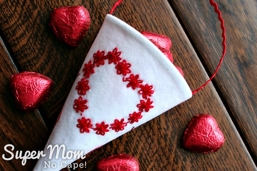 White Fabric Treat Cone with Red Floral Embroidered Heart filled with candy laying on a wooden table