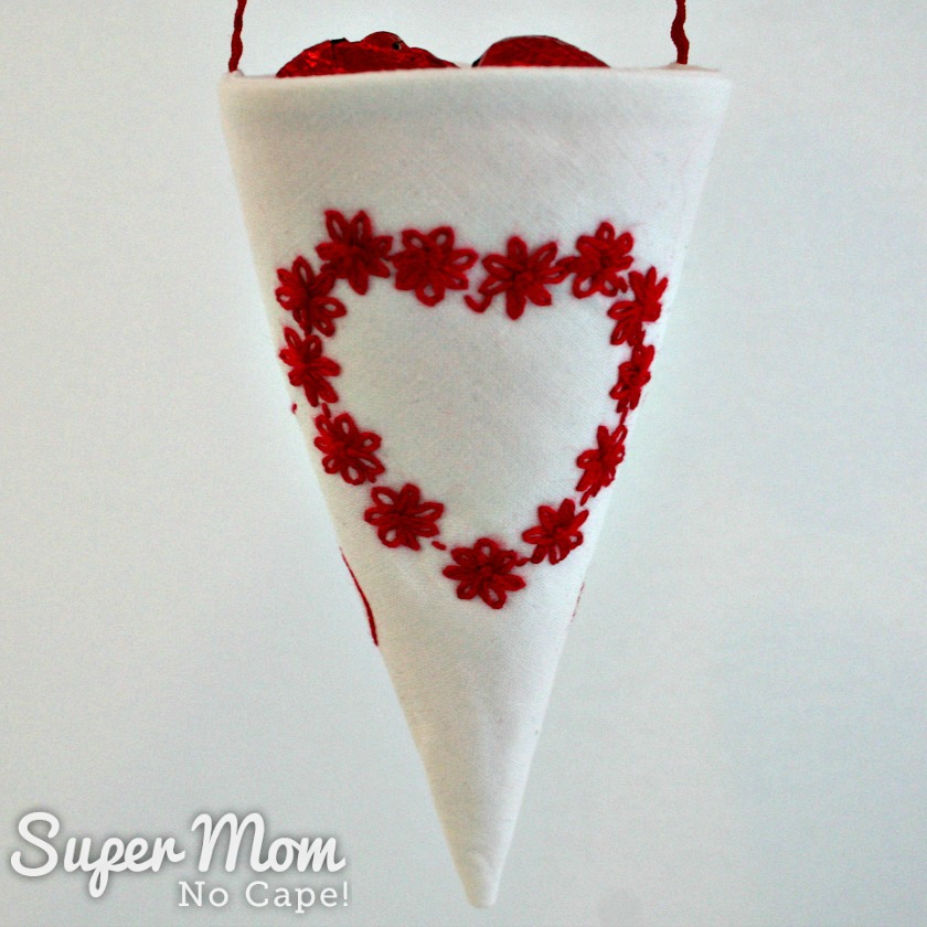 Front of the white fabric treat cone with red heart made of embroidered lazy daisy flowers 