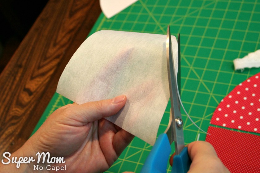 Photo of trimming an eight of an inch off interfacing all the way around using a blue handled scissors.