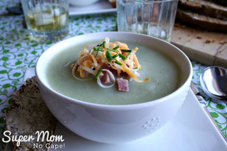 Bowl of potato soup garnished with chopped ham, grated cheese and chives