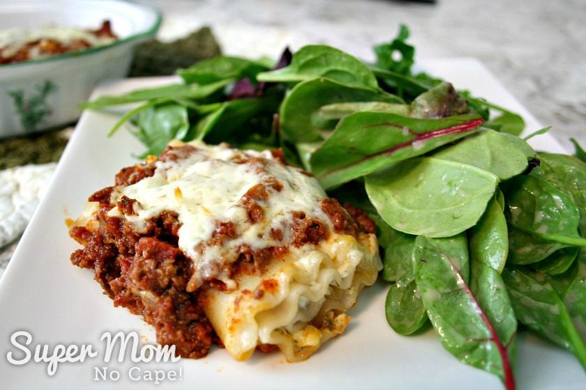Make these Easy Lasagna Roll Ups for supper tonight or freeze them to have for those nights when life gets a little crazy and you don't have time to cook. Freezer cooking is a sanity saver and this recipe is a family favorite that you'll want to make again and again. #recipes #freezercooking #lasagnarecipes #lasagna #pastarecipes Lasagna Roll Up on white plate with mixed green salad