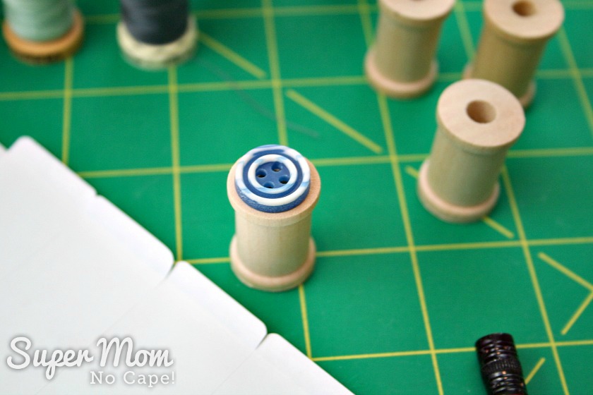  Small blue button sitting on top of miniature wooden spool