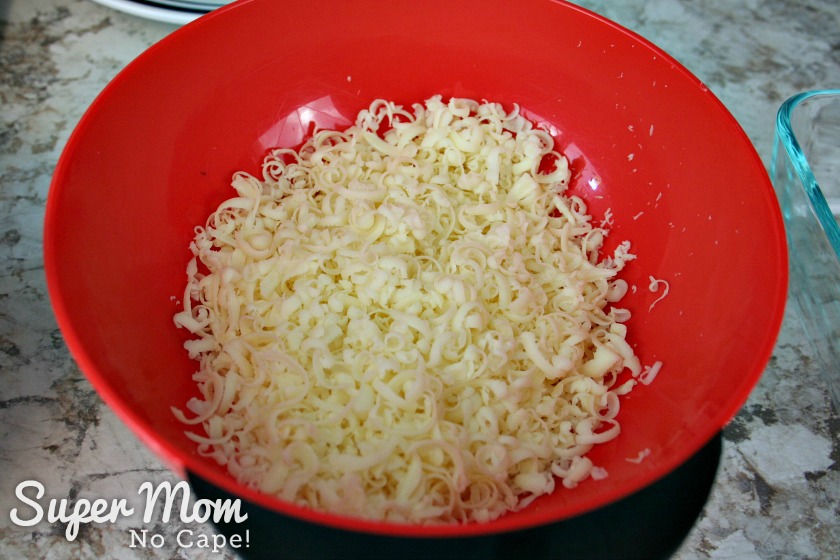 Make these Easy Lasagna Roll Ups for supper tonight or freeze them to have for those nights when life gets a little crazy and you don't have time to cook. Freezer cooking is a sanity saver and this recipe is a family favorite that you'll want to make again and again. #recipes #freezercooking #lasagnarecipes #lasagna #pastarecipes Red bowl with grated mozzarella cheese for Lasagna Roll Ups