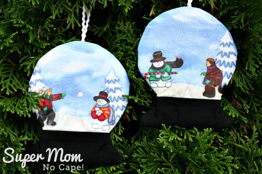 Two fabric vinyl snowglobes hanging on evergreen