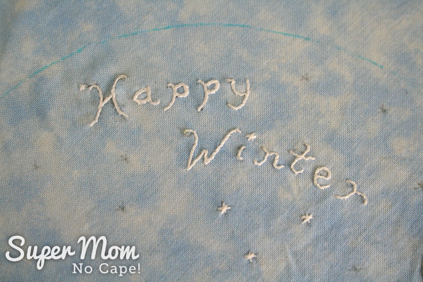 Embroidered words Happy Winter with white floss on blue fabric
