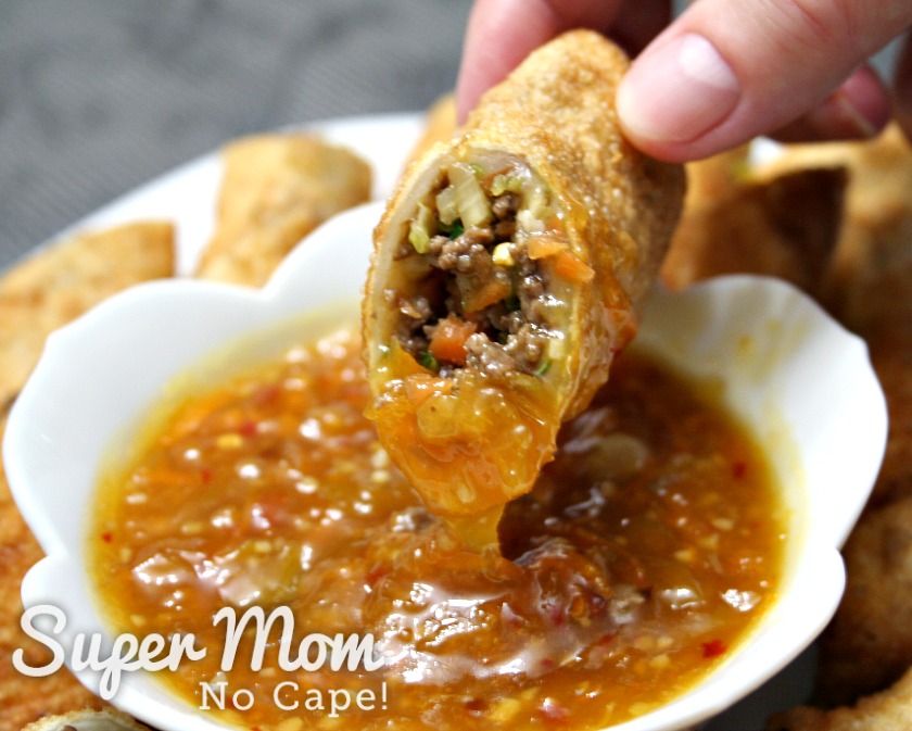 Homemade egg roll being dipped into a bowl of orange sauce