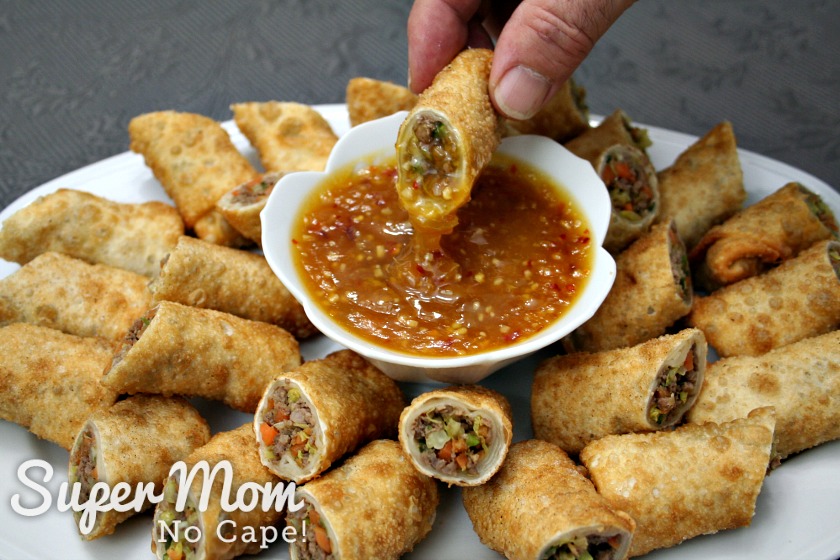 Platter of sliced egg rolls with bowl of orange sauce in the middle