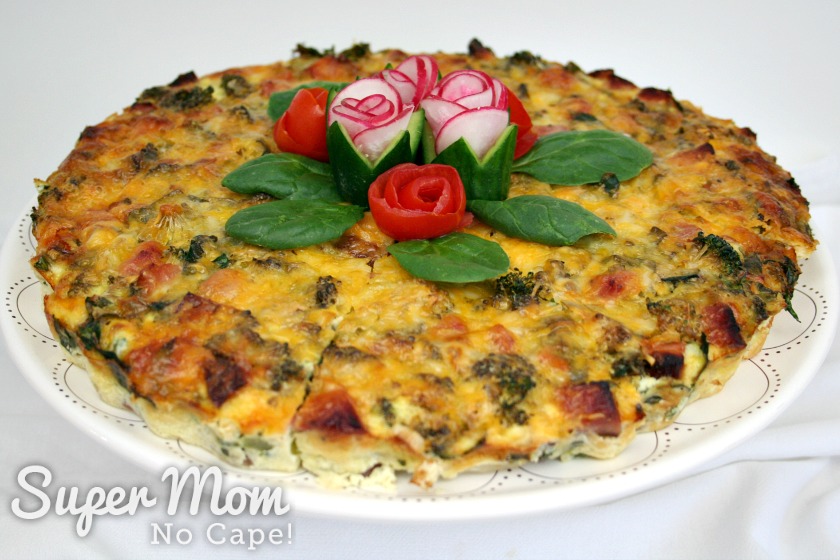 Cake plate with slices of crustless quiche arranged in a circle garnished with tomato and radish roses