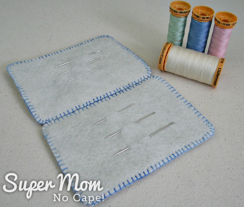 Open Needles needle book with various size needles beside 4 spools of thread