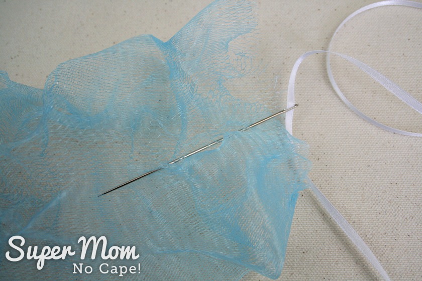 Weaving the needle through the blue mesh of the unraveled shower puff