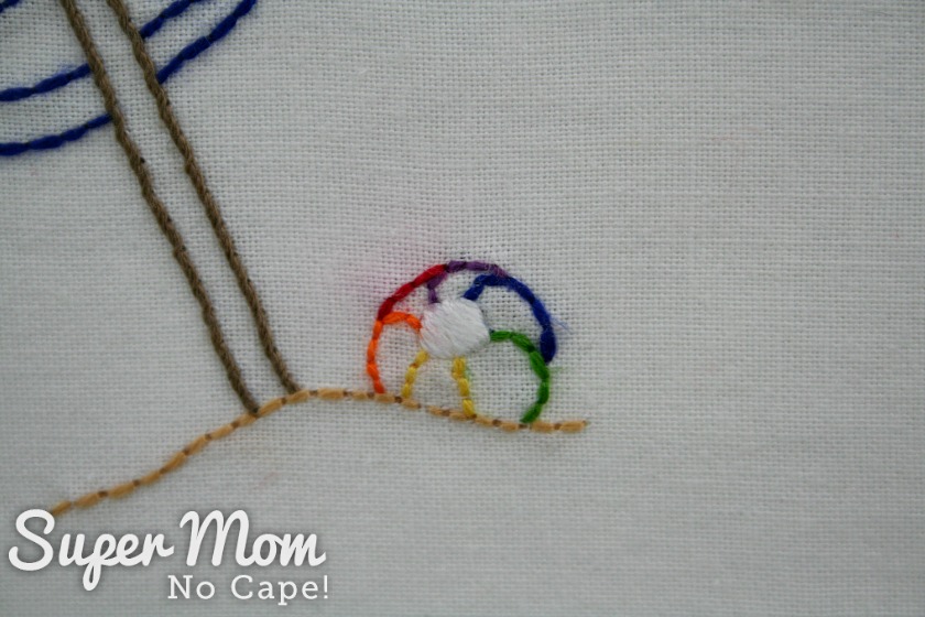 Multicolored embroidered beach ball sitting on sand beside beach umbrella