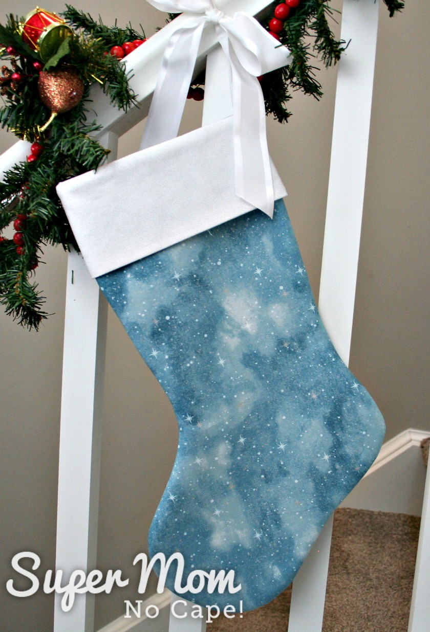 Blue Star Stocking with white cuff hanging from a bannister decked with holiday greenery.