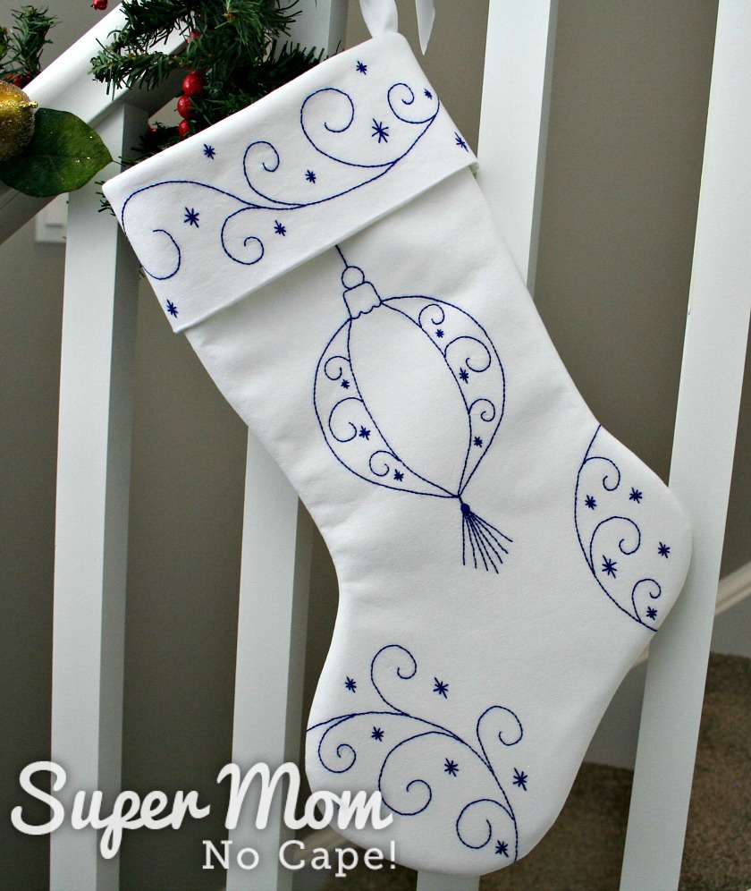 White stocking with blue embroidery hanging from a bannister.