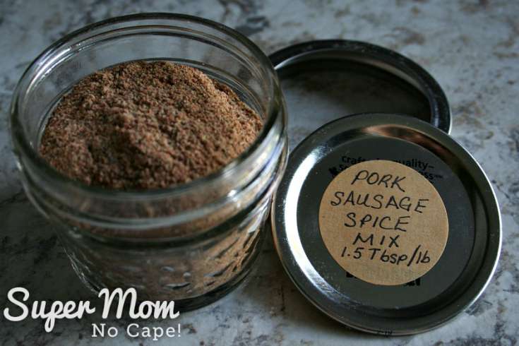 Quarter cup mason jar with Homemade Pork Sausage Meat spice mix beside a labelled lid and jar ring.