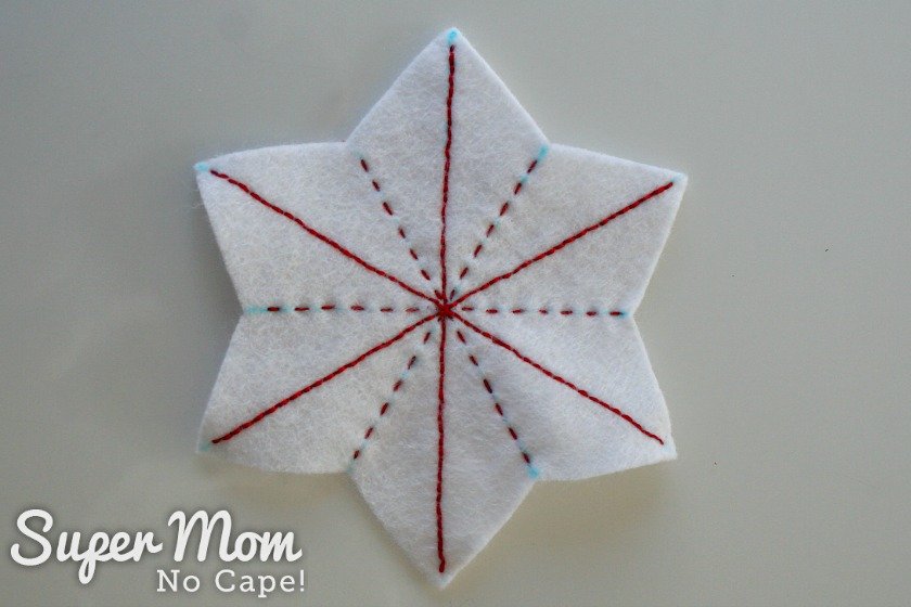 Three lines of backstitching and three lines of running stitch in red on a white felt star.