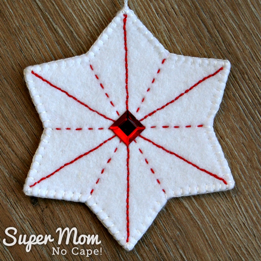 White felt star ornament with red embroidery and a red gem in the center.