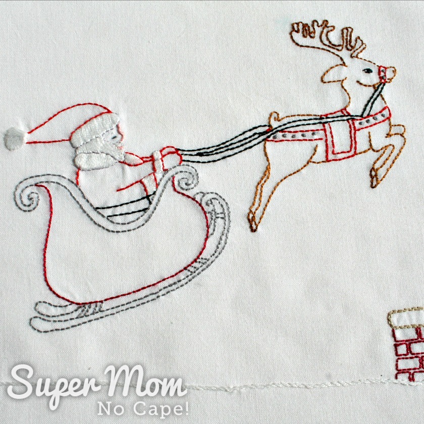 Embroidery of Santa in his sleigh being pulled by a reindeer.