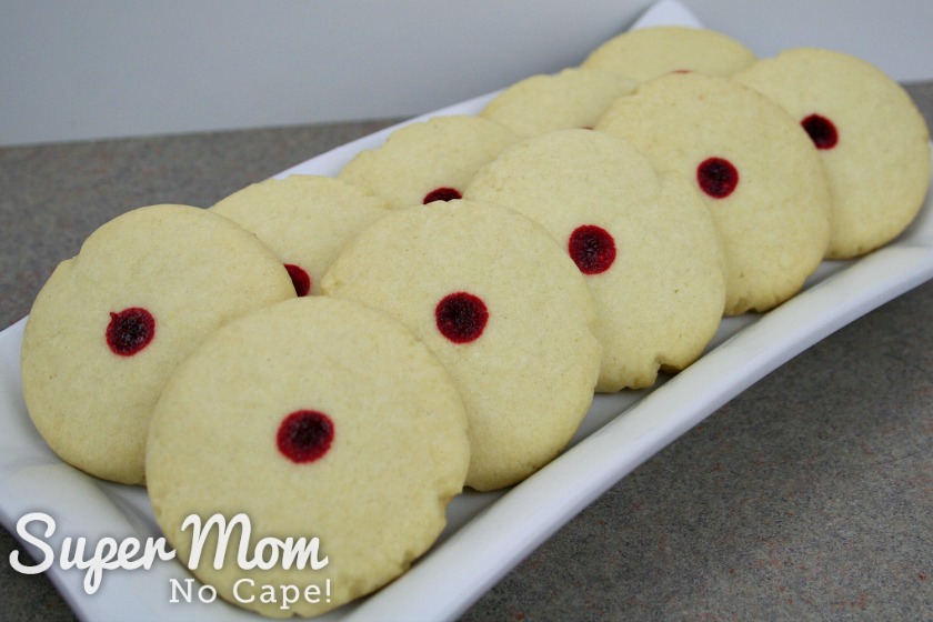 Rectangular plate of red dot almond cookies arranged on it.