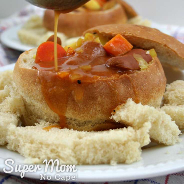 Stream of the wiener stew gravy being poured into stew filled bread bowl