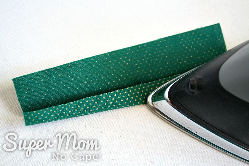 An iron pressing the second crease on the green strip of fabric for the stocking hanger