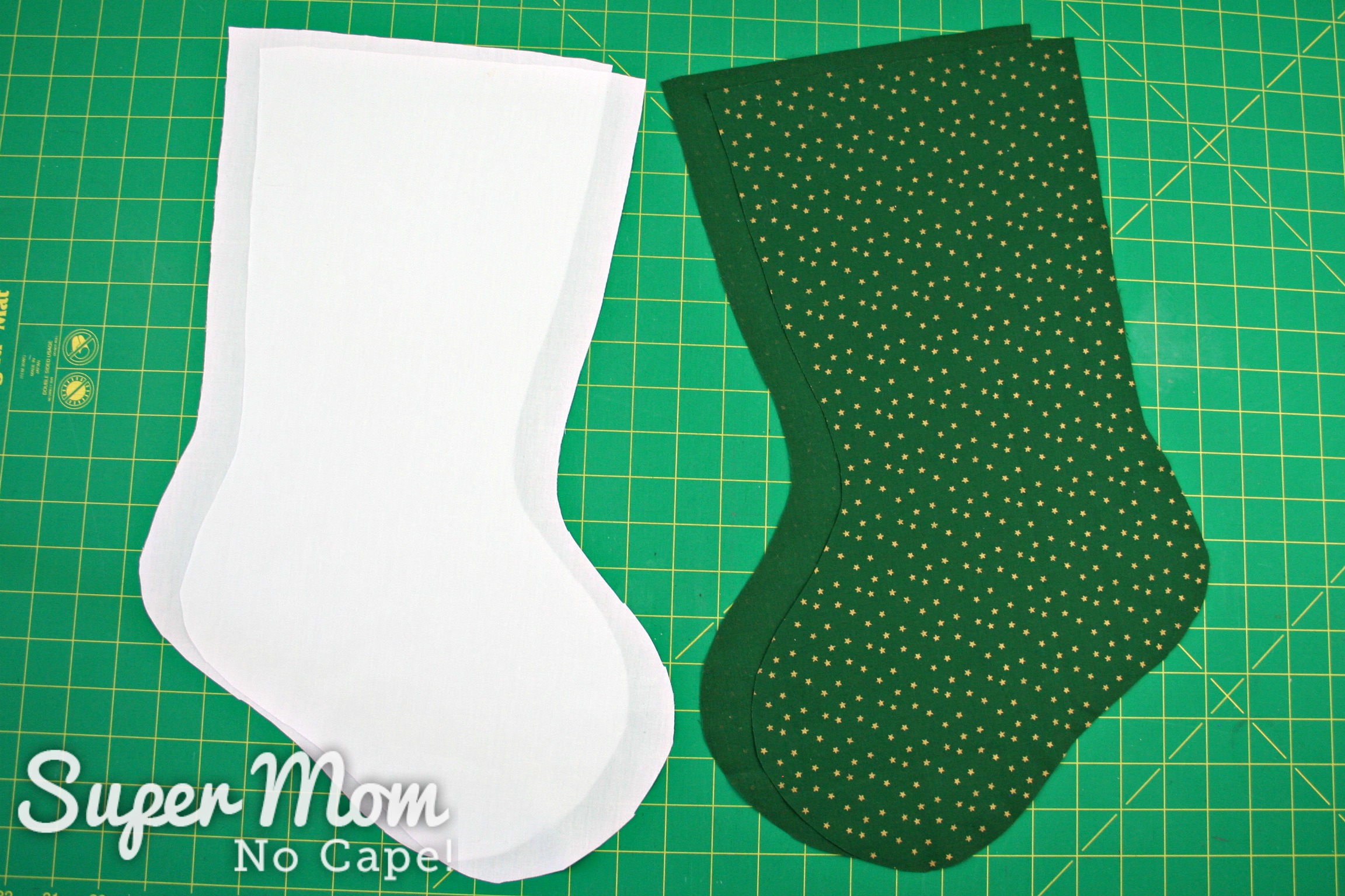 White and green fabric stockings cut out and laying on a green cutting mat.