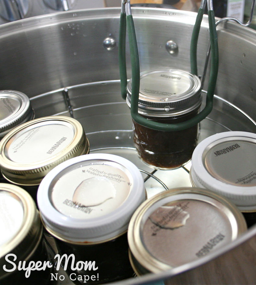 A half pint jar of rhubarb relish being lifted out of a stainless steel canner.