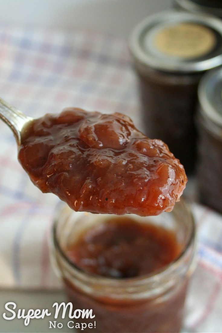 A spoon full of rhubarb relish held over a jar of relish with sealed jars in the background.