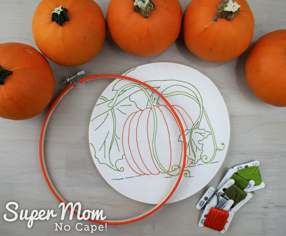 Finished Pumpkin Harvest Time embroidery with orange painted hoop, embroidery floss bobbins and small pie pumpkins