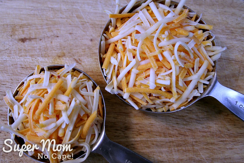 Two measuring cups filled with shredded cheese. In total, the cups measure 1.5 cups of cheese.