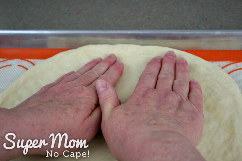 A person patting the pizza dough into a circle.
