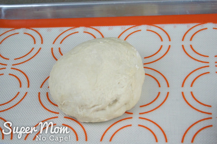 A picture of a ball of pizza dough on a baking tray lined with a silicone baking mat.