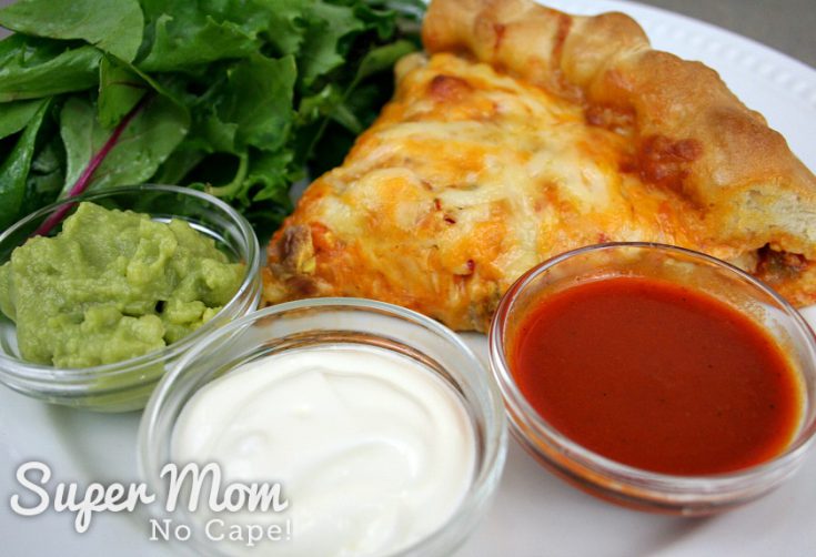 A slice of turkey enchilada tart at top right corner with a spinach salad at top left. Three dipping sauces are at the bottom of the picture, from left to right: guacamole, sour cream and enchilada sauce.