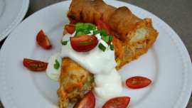A slice of turkey enchilada tart topped with sour cream, green onions and chopped cherry tomatoes.