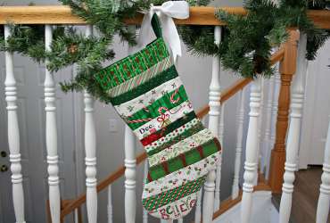 Photo of a Quilt As You Go Christmas Stocking made with a variety of green, white and red print fabrics hanging from a garland wrapped bannister.
