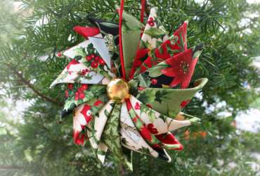 Photo of a Prairie Point Star Ornament made with multiple Christmas fabrics hanging in a pine tree.